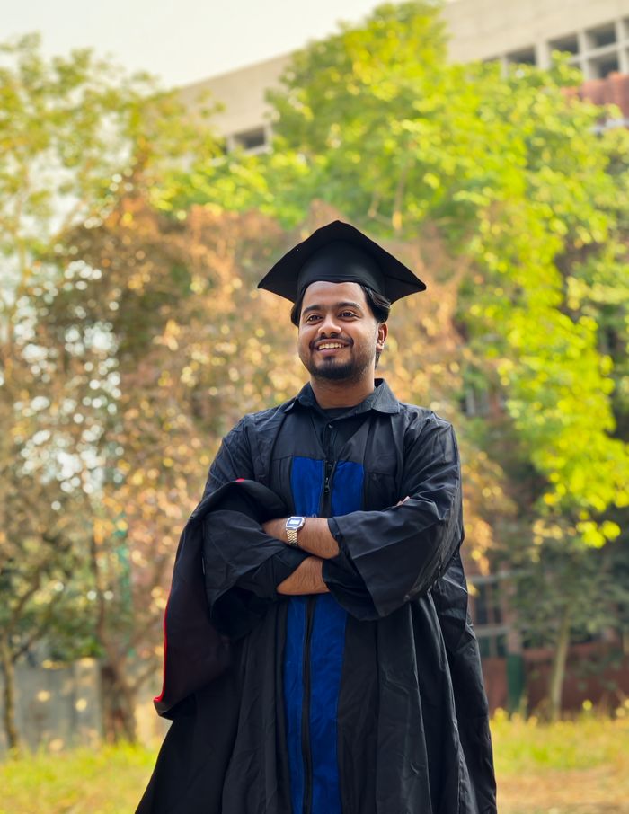 Young graduate in cap and gown smiling outdoors in Savar, Bangladesh.