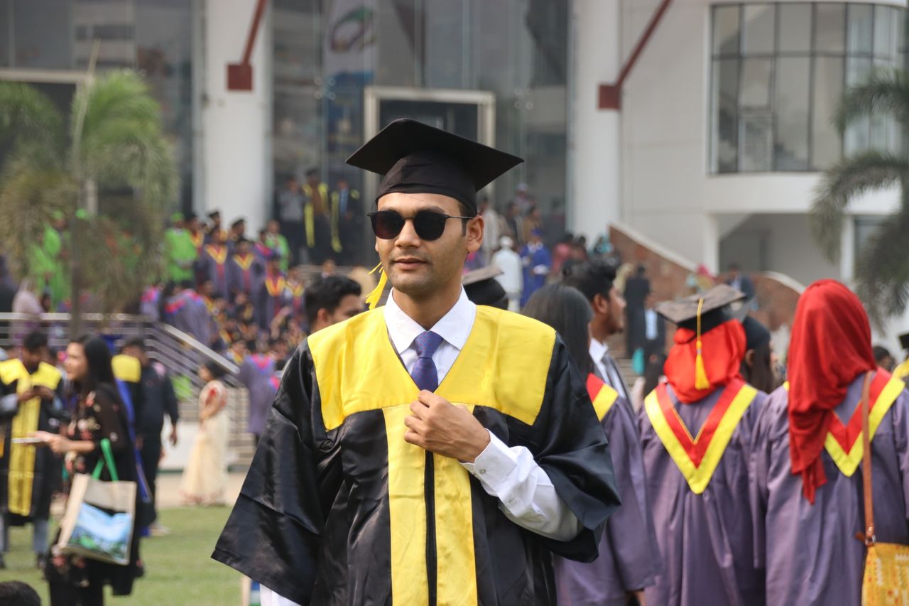 Graduates celebrate their university graduation in traditional attire outdoors on campus.